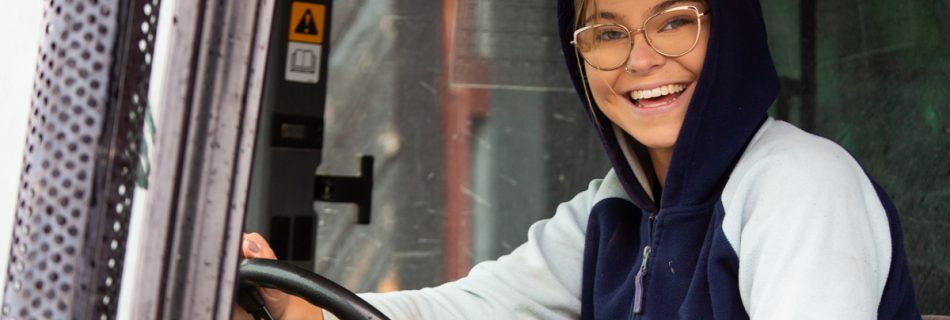 Ung kvinna i hoodie som kör traktor